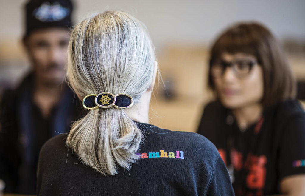 Tre personer i samtal. Kvinna med grått hår i hästsvans, och t-shirt med Samhalls logga, har ryggen mot kameran.