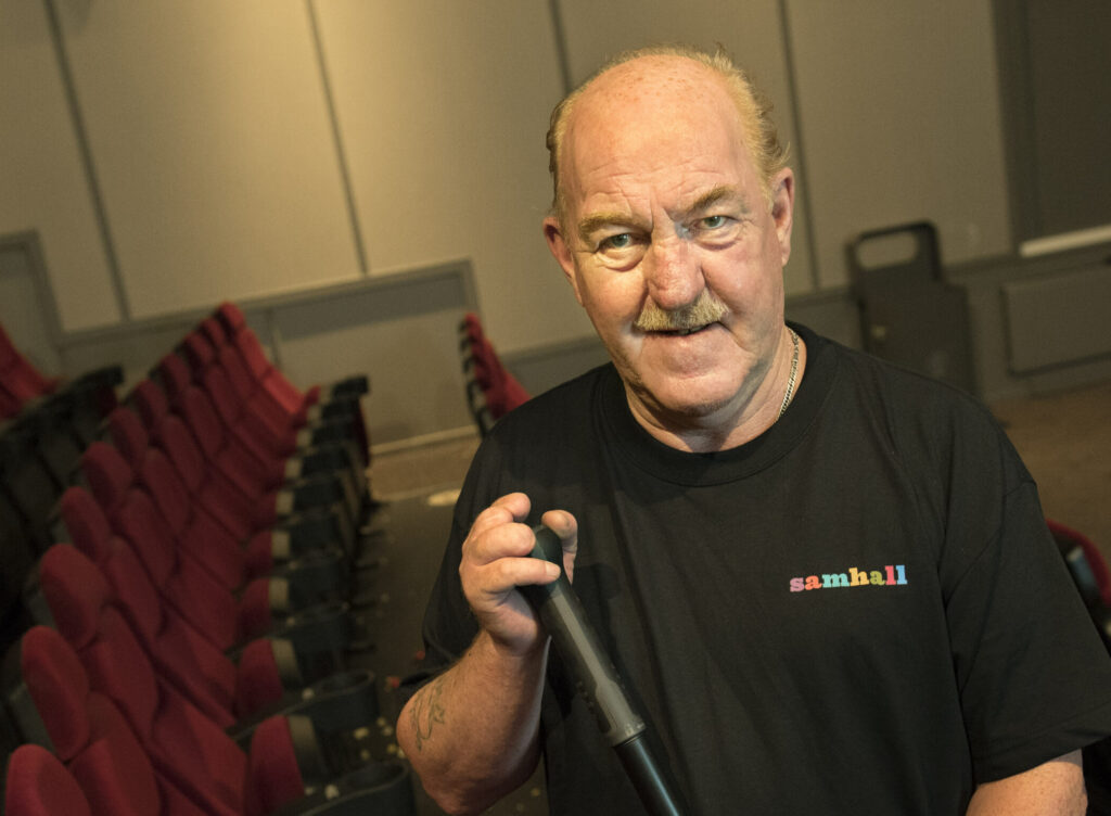 Manlig lokalvårdare i biosalong. Han står bland röda stolar i långa rader.