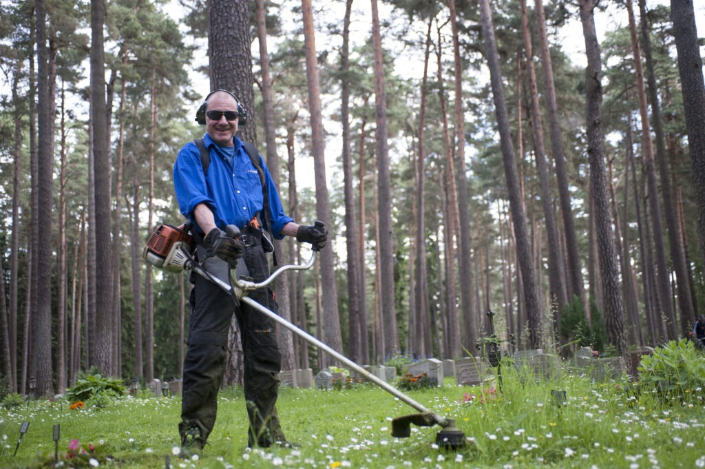Man i solglasögon och hörselkåpor arbetar med grästrimmer.