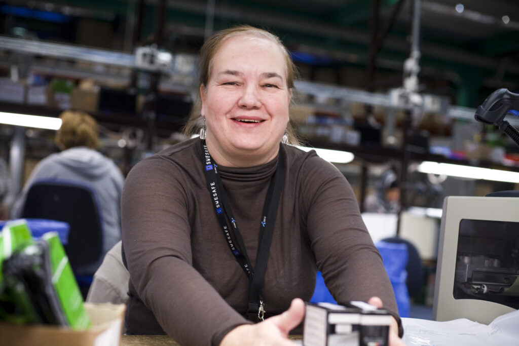 Kvinna i uppsatt hår och brun T-shirt. Hon ler och tittar in i kameran.