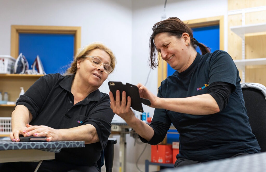 Två kvinnor på Samhalls tvätteri i Vimmerby. Den ena kvinnan visar den andra kvinnan något i mobilen.