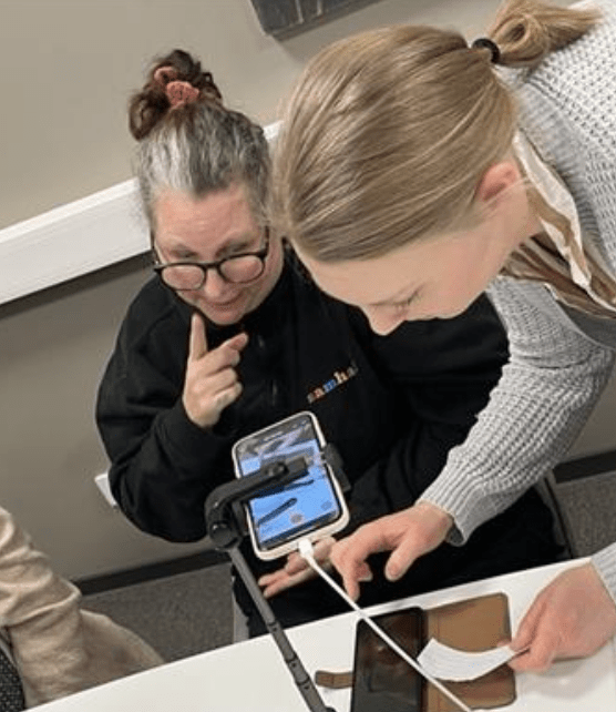 Sanna sitter vid ett bord och användningstestar Portalen. Teckenspråkstolken är i mobilen.