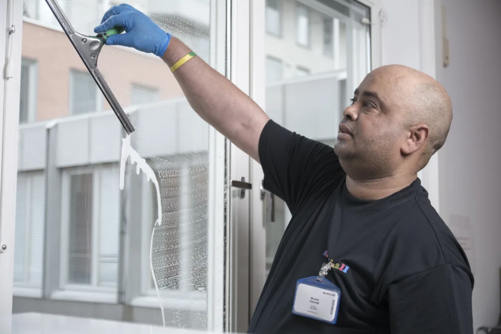 En man putsar fönster. Han står inomhus och använder en fönsterskrapa.