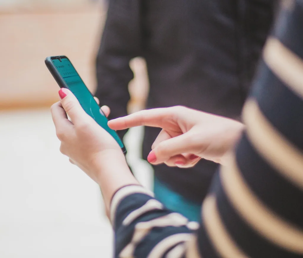 Kvinna håller i mobil och pekar på skärmen. Hon har rött nagellack och bär randig tröja.