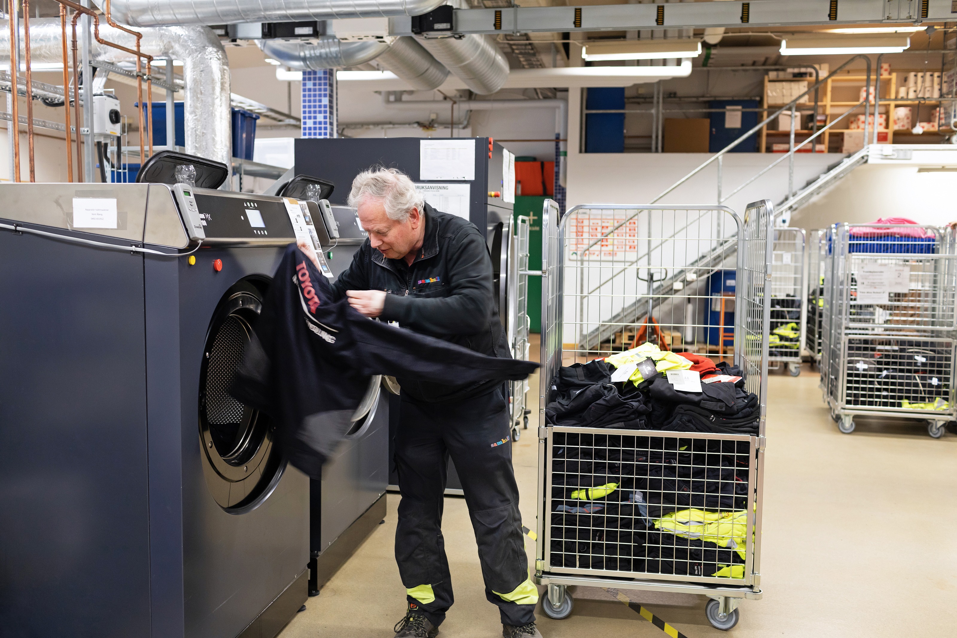 Man i svarta Samhallkläder fyller en tvättmaskin på ett tvätteri.