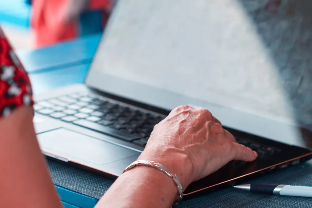 En kvinna skriver på en laptop. Hon bär en kortärmad tröja och har ett armband på höger arm.