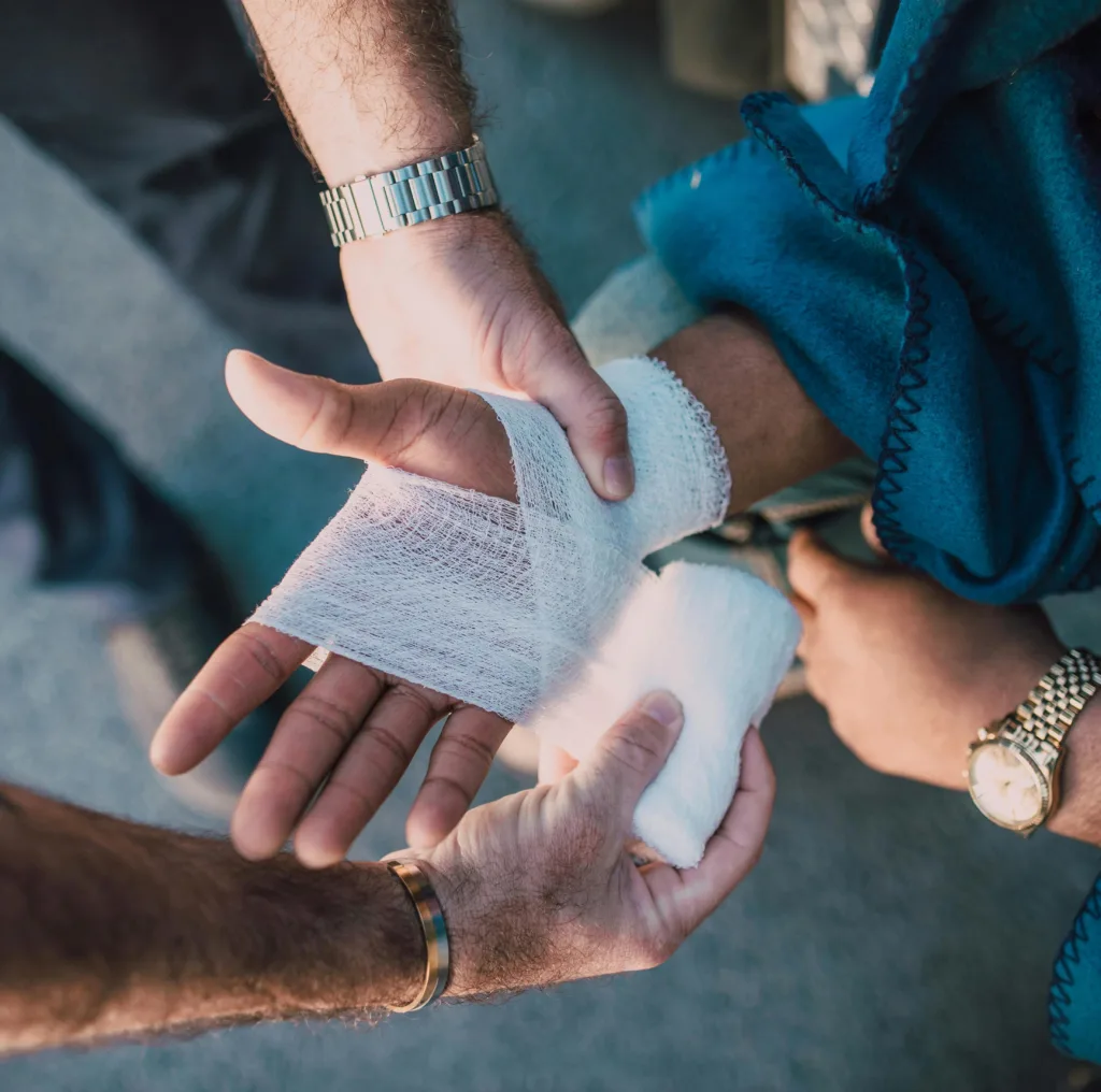 Någon har skadat sin hand. En man lägger förband runt handen.