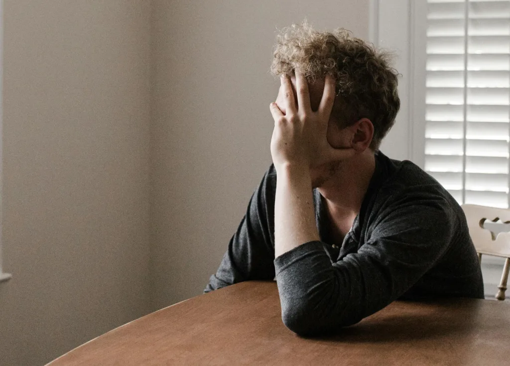 En blond och lockig man sitter vid ett bord. Han lutar huvudet i händerna, så man ser inte hans ansikte.