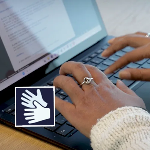 Händer skriver på dator med symbol för teckenspråkstolkning.