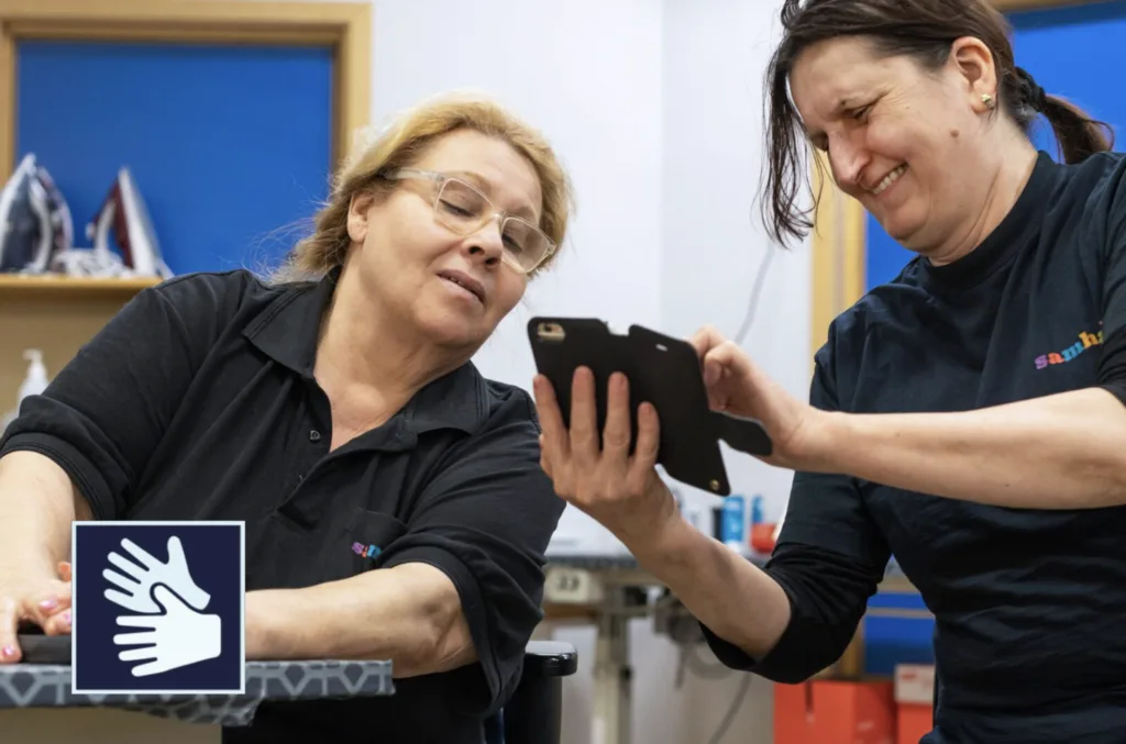 Två kvinnor tittar på en mobiltelefon. I nedre vänstra hörnet syns en ikon för teckenspråkstolkning.