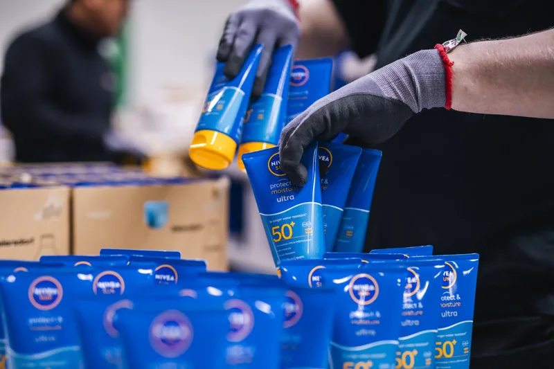 En samhallsanställd med handskar som packar solkräm i ett paket.