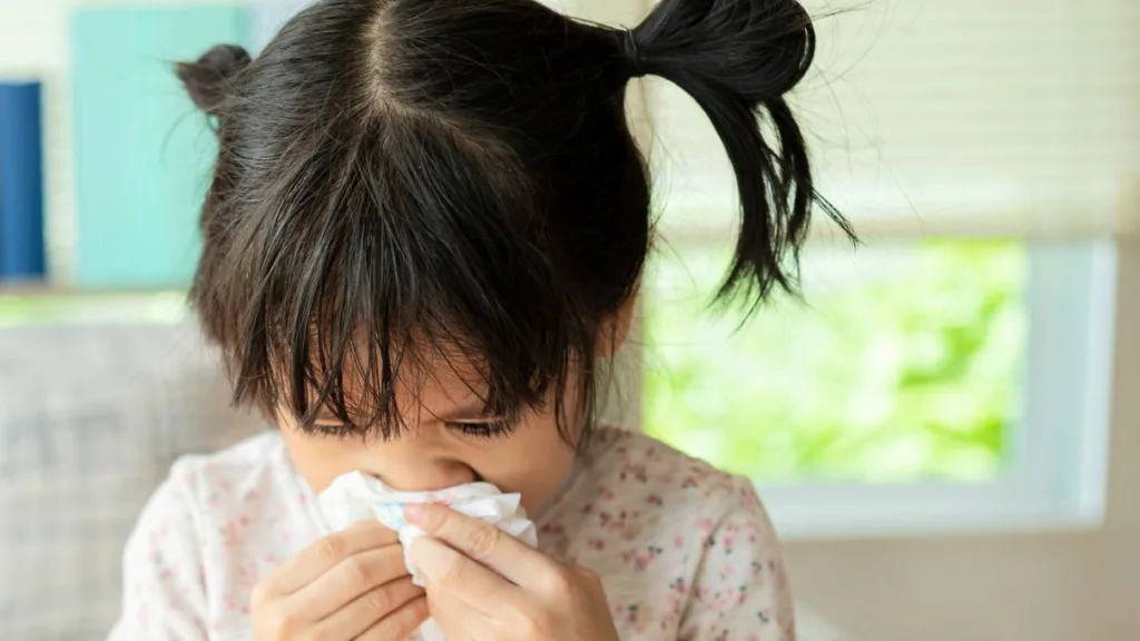 Liten flicka i rufsiga hårtofsar. Hon snyter sig.