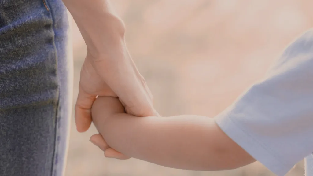 Inzoomade händer - en kvinna håller ett litet barn i handen.