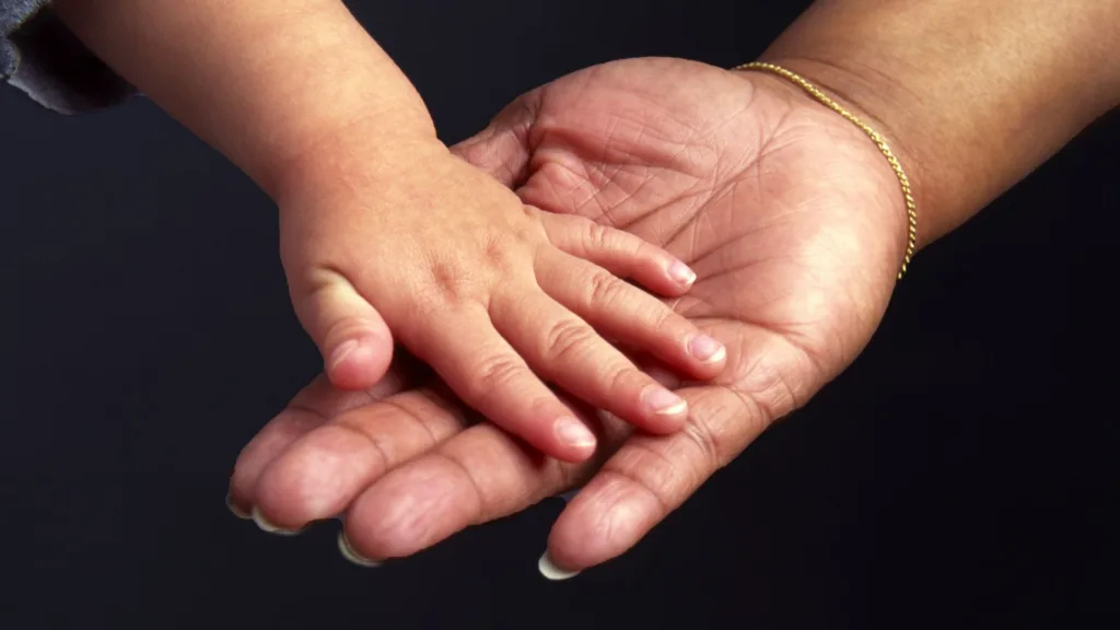 Närbild: Ett litet barn lägger sin hand i en vuxen kvinnas hand.