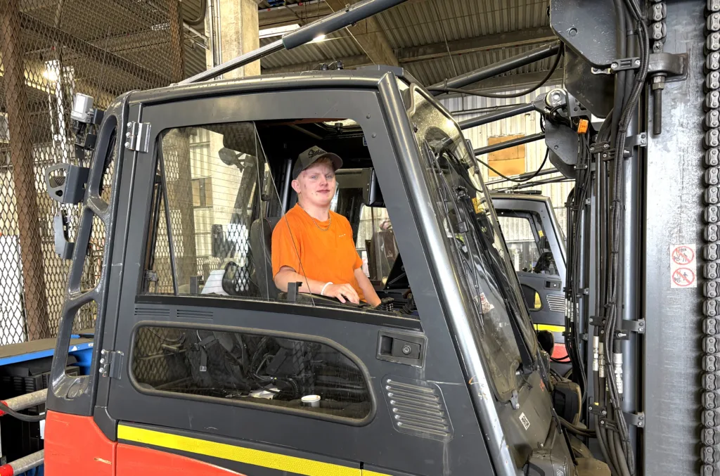 Gustav sitter i en truck. Han har keps och en orange T-shirt.